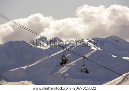 A ski lift in Dolomite mountanins, with completely white mountain tops fully covered with snow in the background and a big cloud above