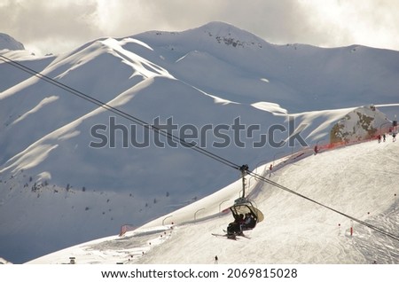 A ski lift in Dolomite mountanins, with completely white mountain tops fully covered with snow in the background