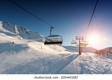 Ski lift empty ropeway on hilghland alpine mountain winter resort on bright sunny evening . Ski chairlift cable way with people enjoy skiing and snowboarding. Sunset sky backlit shining on background