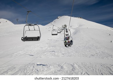 Ski lift empty ropeway on hilghland alpine mountain winter resort on bright sunny evening . Ski chairlift cable way with people enjoy skiing and snowboarding.