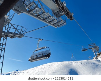 Ski lift empty ropeway on alpine mountain winter resort on bright sunny day. Ski chairlift cable way skiing and snowboarding. European Alps snowcapped mountain. - Powered by Shutterstock