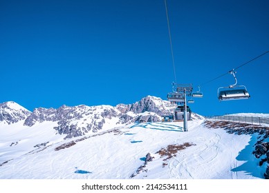 Ski lift reaching towards station. Chairlift over beautiful snow covered mountain range against blue sky. Scenic view of winter sport.