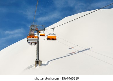 Ski lift ropeway on hilghland alpine mountain winter resort on bright sunny day. Ski chairlift cable way with people enjoy skiing and snowboarding.Banner panoramic wide view of downhill slopes