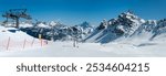 Ski lift and ski runs and pistes in Arabba ski resort in Dolomites in Italy in winter. Easy ski slopes and unrecognizable skiers on the chairlift. Rocky mountain range in the background. Wide panorama