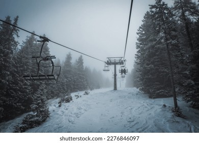 Ski lift transports skiers and snowboarders in foggy day at snowy mountain. Frozen funicular. Pinzolo and Madonna di Campiglio ski resort. January 2023 - Powered by Shutterstock