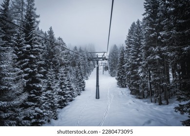 Ski lift transports skiers and snowboarders in foggy day at snowy mountain. Frozen funicular. Pinzolo and Madonna di Campiglio ski resort. January 2023 - Powered by Shutterstock