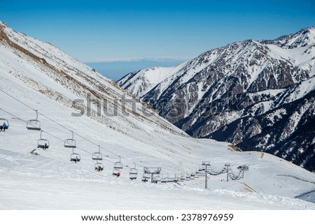 Ski lifts, skiers and snowboarders on pistes in beautiful winter scenery with mountain range in the background, Kazakhstan, Shymbulak