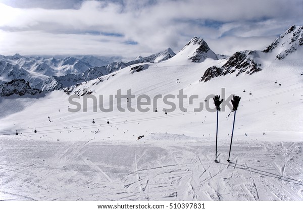 Ski poles with ski gloves, gondola\
cable car, ski tow, and skiers on the slope on Tiefenbach glacier\
in Solden ski resort in Otztal Alps, Tirol,\
Austria