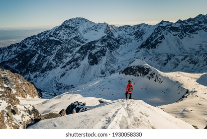 Ski tourer ascending a snow slope carrying skis on his backpack. Climber in a reed jacket climbs a mountain against a blue sky. On top of a mountain and enjoying view. Adventure concept