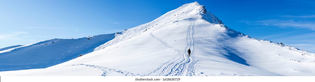 ski tourer climbing the steep mountain. snow shoe hiker following the trails on a sunny day with blue sky - Powered by Shutterstock