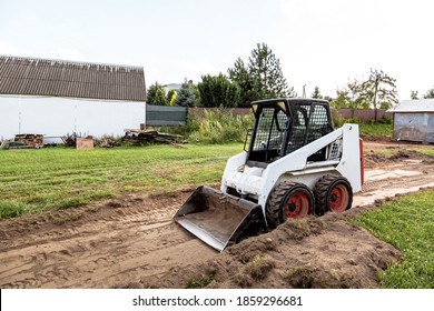 A skid steer loader clears the site for construction. Land work by the territory improvement. Machine for work in confined areas. Small tractor with a bucket for moving soil, turf and bulk materials.