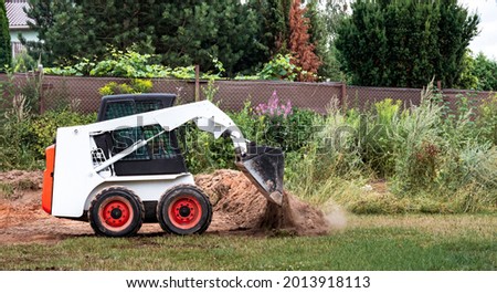 A skid steer loader clears the site for construction. Land work by the territory improvement. Machine for work in confined areas. Small tractor with a bucket for moving soil, turf and bulk materials.