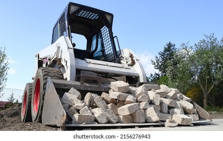 Skid steer loader for construction site with loading bucket filled with bricks.