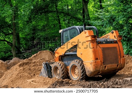 A skid steer loader shovels soil in a park