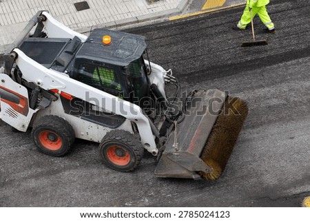 skid steer loader with sweeper attachment cleaning asphalt road
