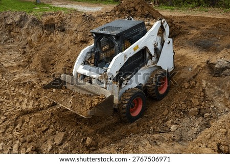 Skid steer loader transporting soil inside a foundation pit, leveling and moving earth during early-stage construction. 