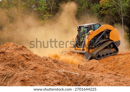 Skid steer works to clear plot of land in forest, kicking up dust moving soil