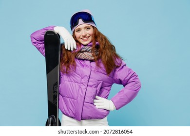 Skier cheerful satisfied happy sporty woman wear warm purple padded windbreaker jacket goggles mask spend extreme weekend in mountains hold ski stand akimbo isolated on plain blue background studio. - Powered by Shutterstock