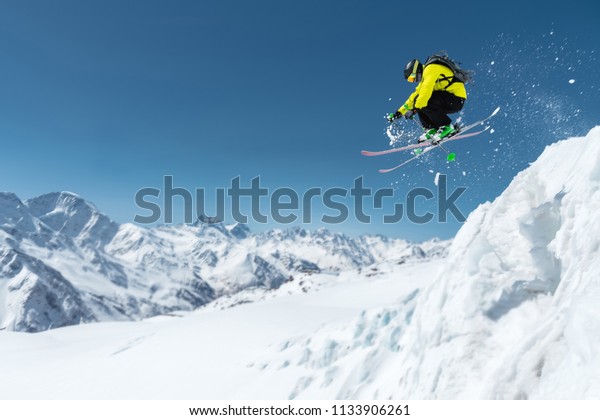 A\
skier in full sports equipment jumps into the precipice from the\
top of the glacier against the background of the blue sky and the\
Caucasian snow-capped mountains. Elbrus region.\
Russia