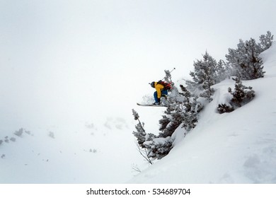   A Skier Is Jumping Stunt In The Snowy Mountains. Skier In Yellow And Blue Ski Suit. Overcast