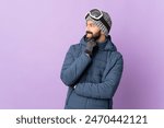 Skier man with snowboarding glasses over isolated purple background looking to the side and smiling