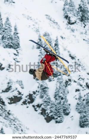A skier performs a complicated trick in jumping big air in snow park at ski resort. A skier in a helmet, light jacket and red trousers does a somersault in the air. Ski freestyle competitions.