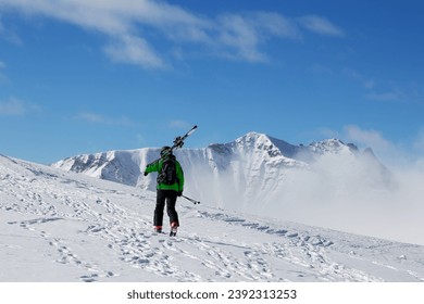 Skier with skis on his shoulder go up to top of mountain in cold sun day. Winter Caucasus Mountains in fog, Georgia, region Gudauri. - Powered by Shutterstock