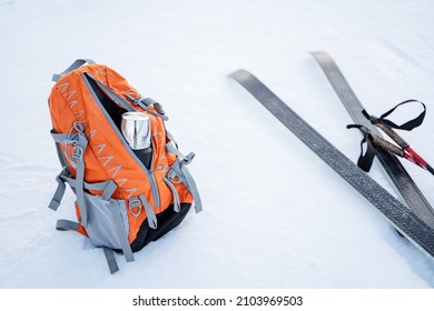 The skier stopped for lunch. The backpack lies on the snow next to a pair of skis and poles. Thermos with tea for a snack. Camping equipment for a winter hike. High quality photo