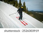 A skier swiftly carves down a snowy slope, the bright red skis contrasting against the white snow and evergreen forest.