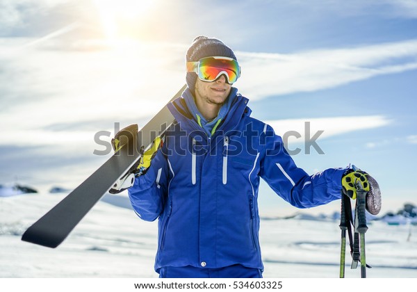 Skier\
watching the horizon holding skiing equipment with sun back light -\
Young athlete in snow mountains for winter vacation - Sport concept\
for a healthy lifestyle - Warm vivid\
filter