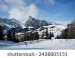 Skiers at the alta badia ski resort with sassongher mountain in the distance, dolomites, south tyrol, italy, europe