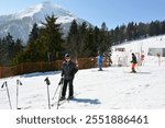 Skiers go down a snowy ski slope in the mountains at a ski resort against the background of forest trees and mountains in the distance