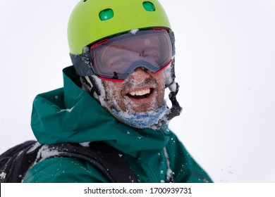 Skier's portrait during a big snowfall. the guy in the bright helmet and glasses at snow blizzard in the mountforest. Happy and smiling Freerider with snow on his face. high-resolution portrait