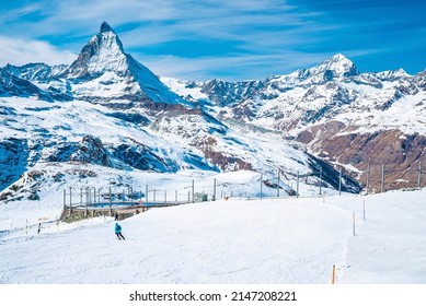 Skiers Skiing On Snow Covered Landscape. Beautiful White Matterhorn Mountain Range Against Sky. People Enjoying Winter Sport In Alpine Region.