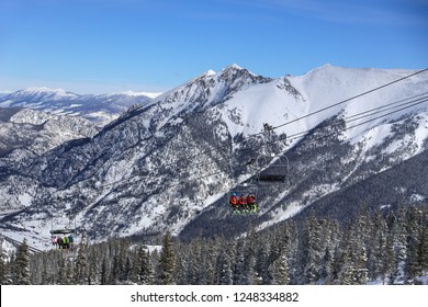 Skiers And Snowboarder Riding A Chairlift High Int He Colorado Rocky Mountains With Winter Snow On A Blue Sky Day At Copper Mountain Ski Resort