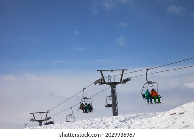 Skiers and snowboarders go up on chair-lift, snowy off-piste ski slope and high mountains in fog at sun winter day. Caucasus Mountains, Georgia, region Gudauri.