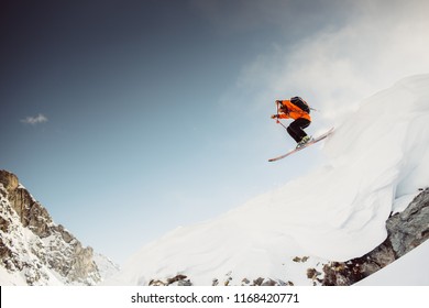 Skiier in the alps jumping down cliff in red jacket with blue sky and sunny weather