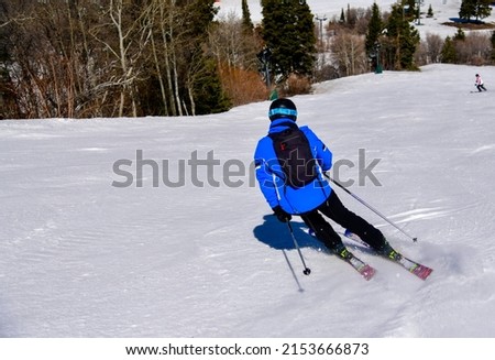 Skiing downhill on a beautiful sunny day at Snowbasin Ski Resort, Utah. Spring conditions in mountains, April month.