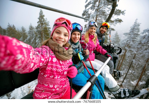 Skiing, ski lift, ski resort - happy\
smiling family skiers on ski lift making\
selfie