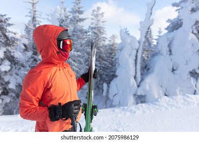 Skiing. Ski portrait of woman alpine skier holdings skis wearing helmet, cool ski goggles and hardshell winter jacket and ski gloves on cold day in front of snow covered trees on ski trail slope