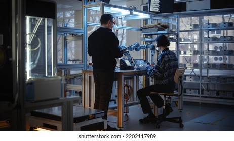 Skilful Male Engineer With Tablet Gives Advice To Young Computer Developer While He Writes Code For Robotic Limb Programme. People Designing Automated Robotic Systems Concept.