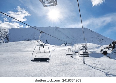 Skilift construction. Empty cable car on mountain slope at ski resort. Winter sport leisure in mountains. Start of snowboard season. Nobody, sunny day, blue sky with clouds. Snowy hills