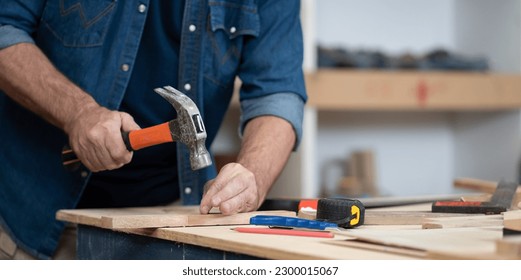 Skill carpenter use hammer hit nail on lumber wood plank. Woodworker repair furniture with manual equipment tool in carpentry workshop. Joiner working on construction or renovation woodworking. - Shutterstock ID 2300015067