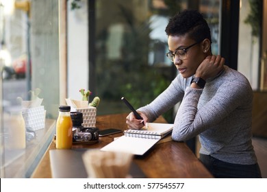 Skilled afro american female administrative manager of company creating schedule of working day for employees organizing job in office during lunch break sitting at table in modern coffee shop