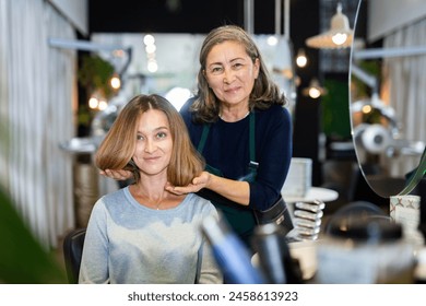 Skilled aged female hairdresser offering modern hairstyling to young woman client visiting professional hair salon. - Powered by Shutterstock