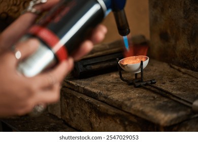 A skilled artisan uses a blowtorch to melt metal, creating exquisite jewels in a cozy workshop. - Powered by Shutterstock