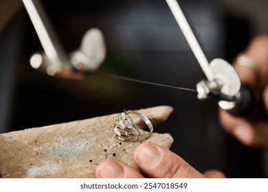 A skilled artisan works meticulously with a delicate silver ring, showcasing craftsmanship. - Powered by Shutterstock