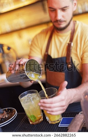 A skilled bartender prepares two refreshing cocktails at a lively bar, showcasing his mixology skills while patrons enjoy the atmosphere during the evening.