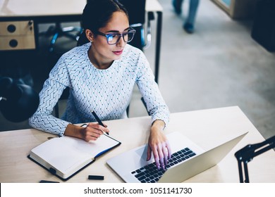 Skilled business woman wear spectacles for vision protection looking at laptop computer monitor during working process, professional female manager searching information on netbook planning in noteboo