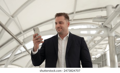 Skilled businessman looking or checking his mobile phone while walking at bridge for going to workplace. Happy manager using telephone to send massage to marketing team and receive good news. Urbane. - Powered by Shutterstock